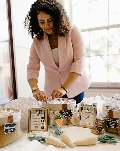 A woman in a pink blazer st和s behind a table displayed with baked goods.